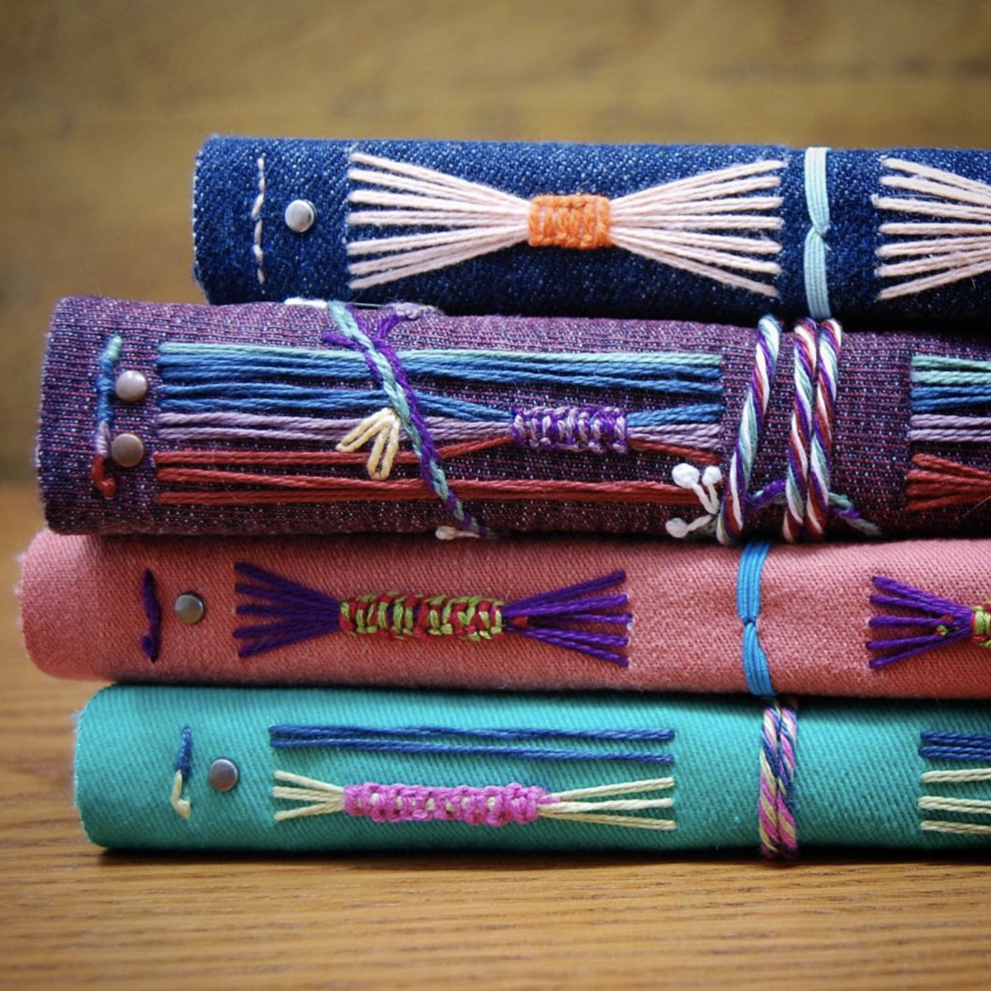 Photo of four books stacked on their side to show elaborate stitching